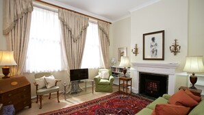 Ein Wohnzimmer mit einem grünen Sofa, einem roten Teppich mit Muster, einem Kamin und einem Fernseher.