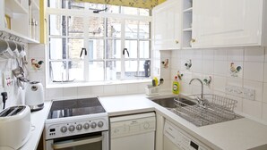 Eine Küche mit weißen Schränken, einem Herd, einem Backofen, einer Spüle und einem Fenster mit Blick auf Gebäude.
