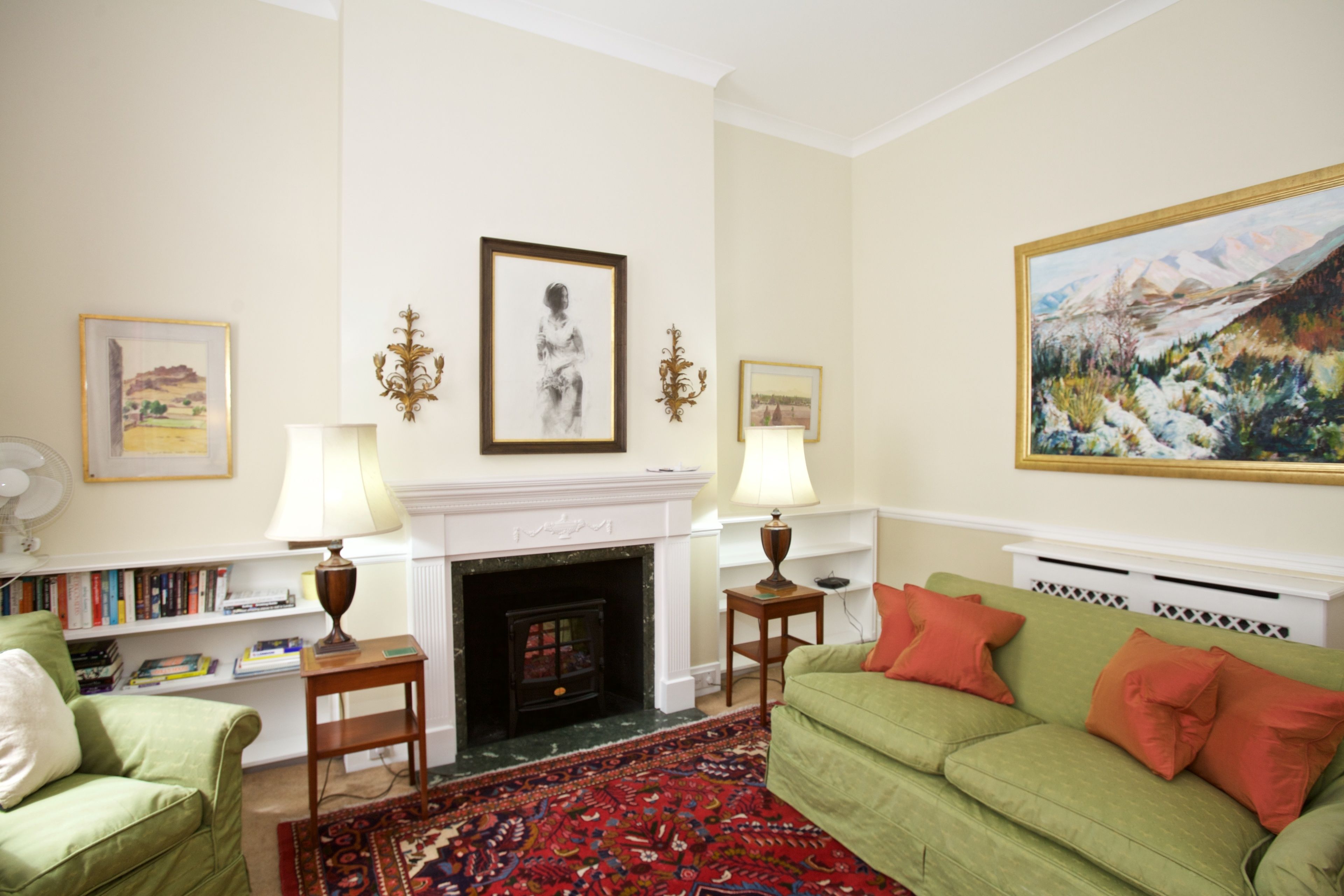 A living room with a fireplace, green sofa, red cushions, and framed artwork on the walls.