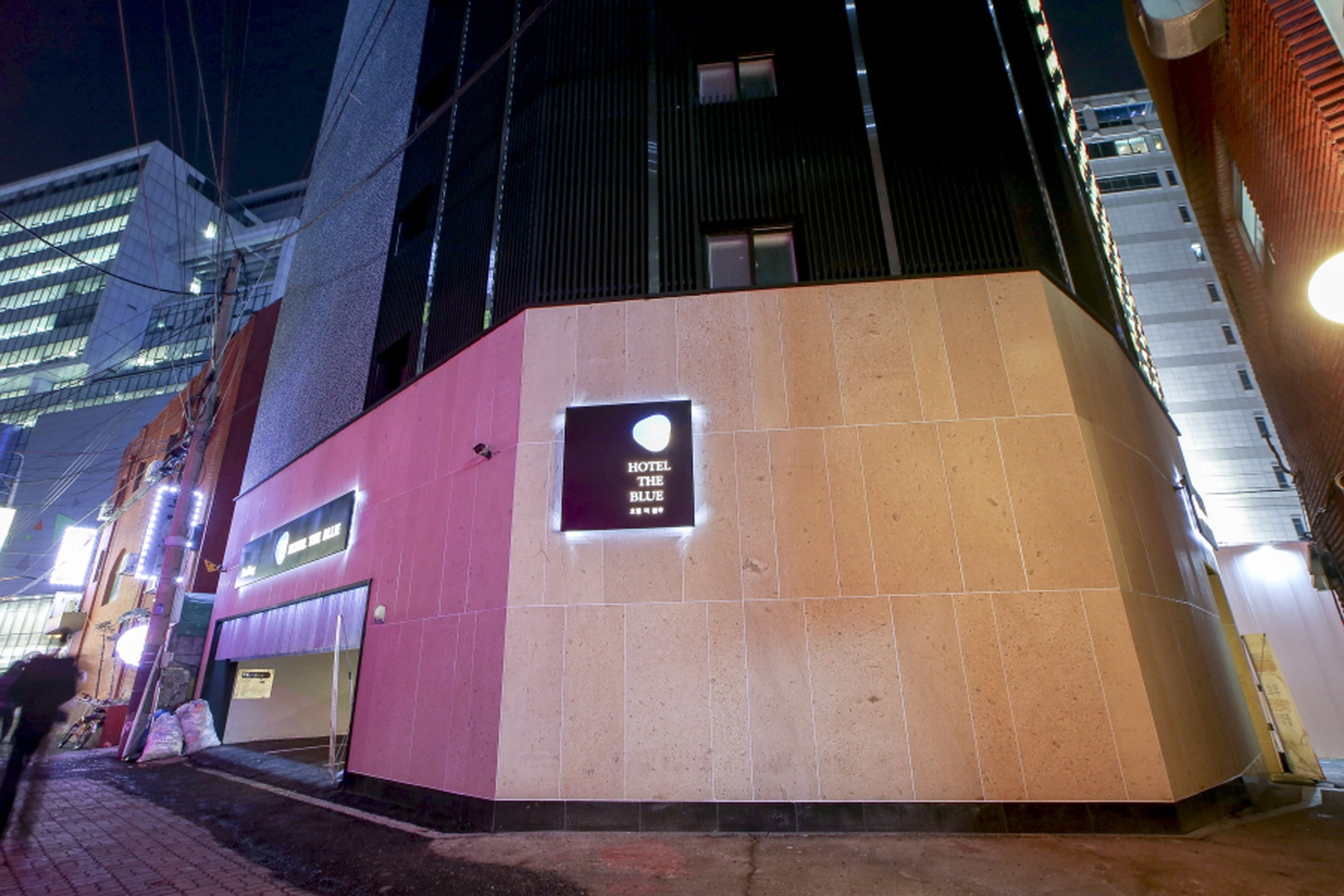 La façade d’un hôtel, avec une enseigne indiquant « HÔTEL THE BLUE » et une entrée bien visible.
