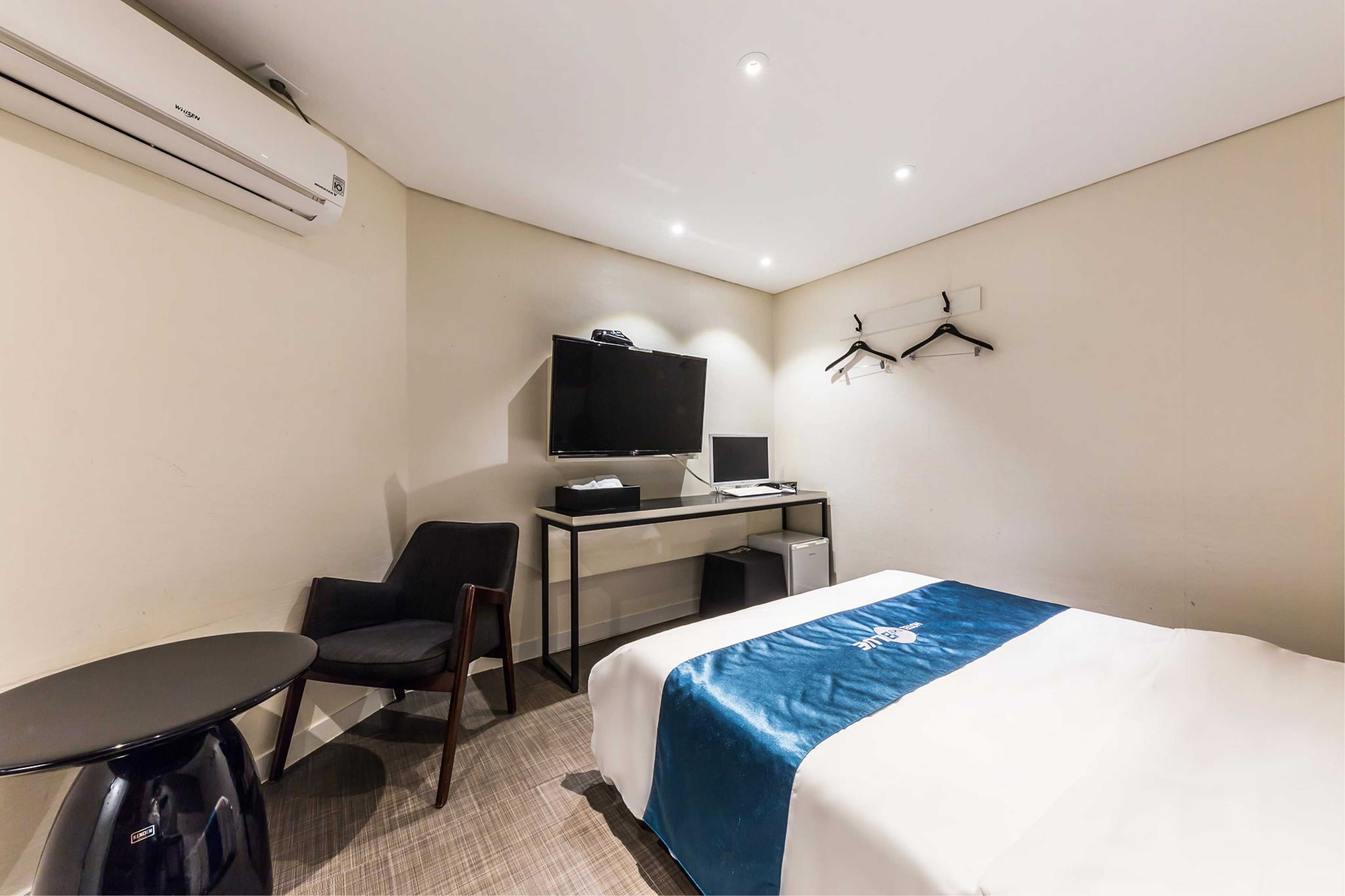 A hotel room with a bed, desk, chair, and a small table.