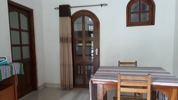 A room with a dining table, chairs, a wooden cabinet, a window, and a door with a curtain.