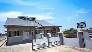 A modern two-story house with a gated entrance, a visible garage, and a signboard advertising property for sale.