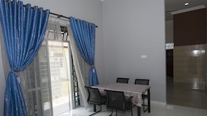 A dining area with a table and chairs, a sliding glass door with curtains, and a view of the outside. - JF Wadi Sofea Homestay (Kuala Terengganu)