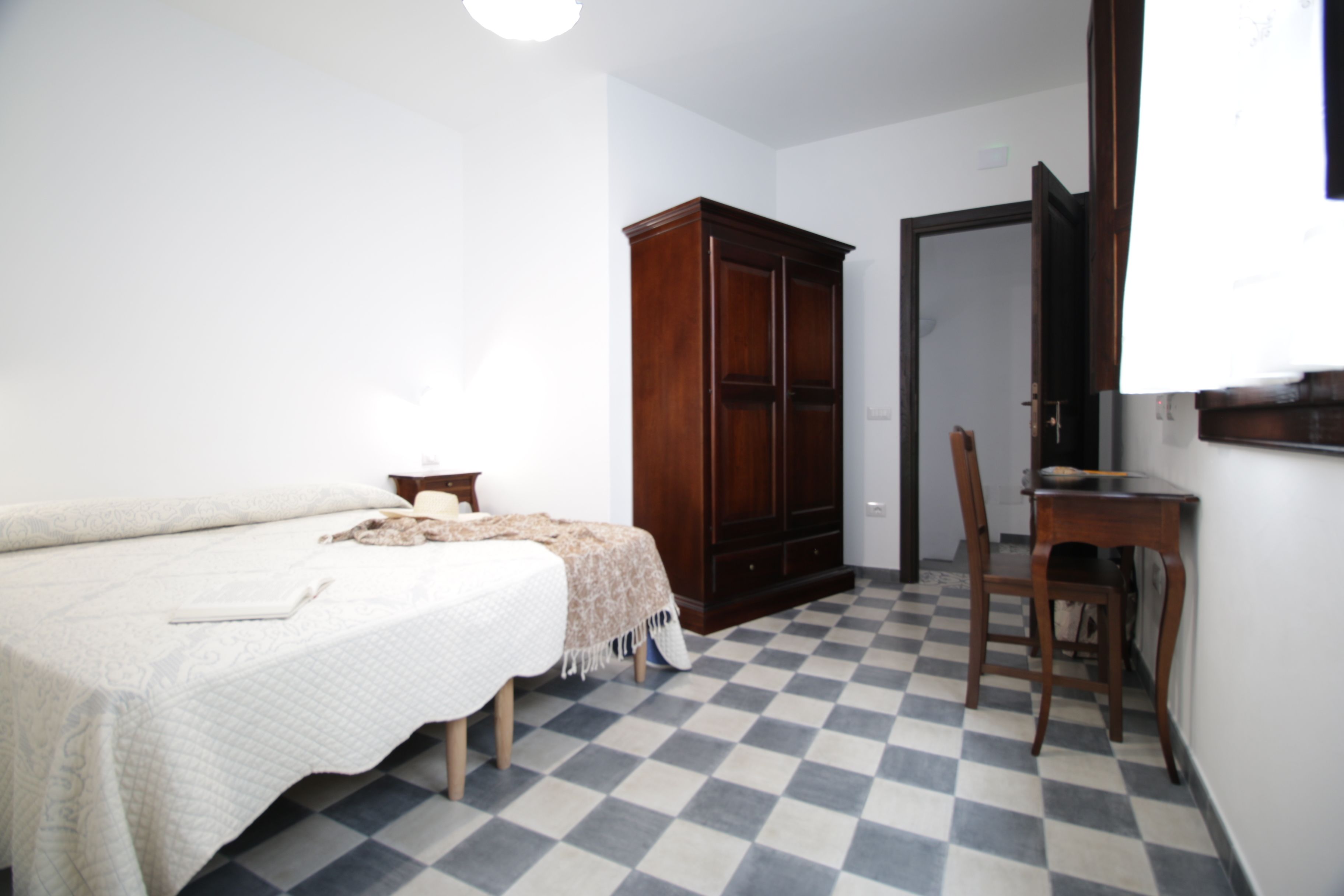 Un dormitorio con cama, un armario de madera, un escritorio con silla y suelo a cuadros.