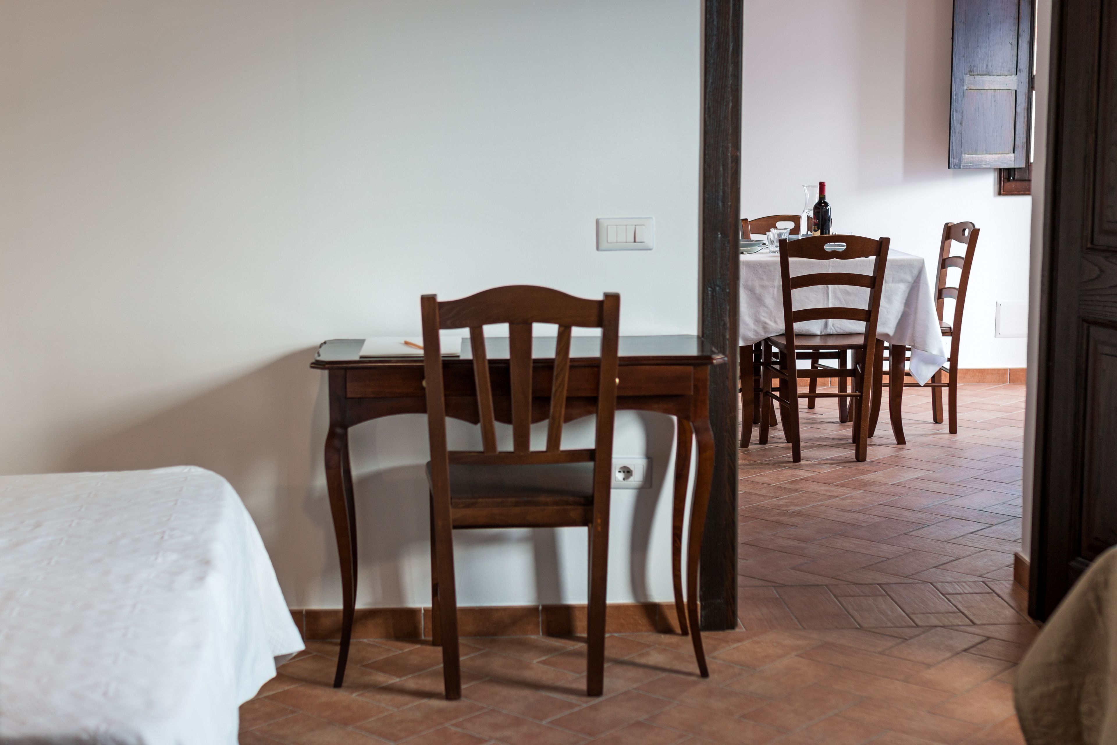 Uma área de refeições com uma mesa de madeira e cadeiras, toalha de mesa branca e piso de azulejos.