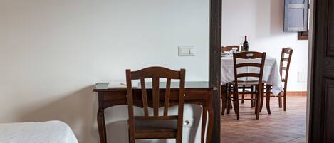 Uma área de refeições com uma mesa de madeira e cadeiras, toalha de mesa branca e piso de azulejos.