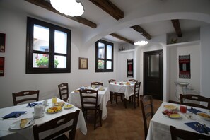 Ein Essbereich mit mehreren Tischen und Stühlen, weißen Tischdecken und Holzbalken an der Decke.