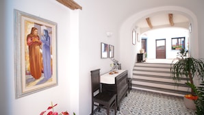 A hallway with a tiled floor, a wooden bench, a desk with a vase, and a framed painting on the wall. - Ghivine Albergo Diffuso (Dorgali)