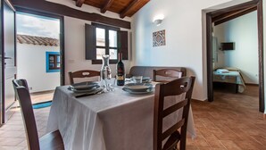 A dining area with a table set for two, a wine bottle, and a view of the outside. - Ghivine Albergo Diffuso (Dorgali)