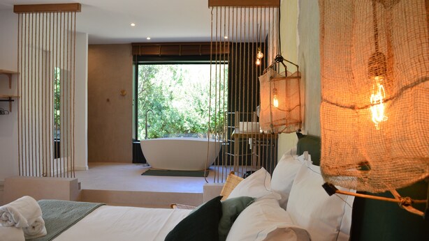 A modern bedroom with a large bed, a bathtub, and a view of greenery outside. - Les Petites Maisons (Sotta)