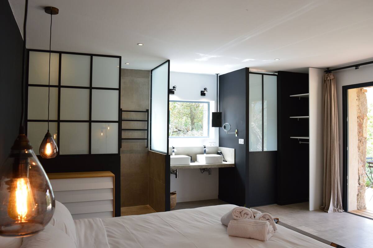 A modern bedroom with a large bed, bedside lamps, a built-in vanity with a mirror, and a view of the outdoors.