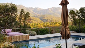 A poolside area with a wooden deck, lounge chairs, and an umbrella. - Les Petites Maisons (Sotta)