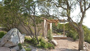 A rustic outdoor area with a pergola, large rocks, and sparse vegetation. - Les Petites Maisons (Sotta)