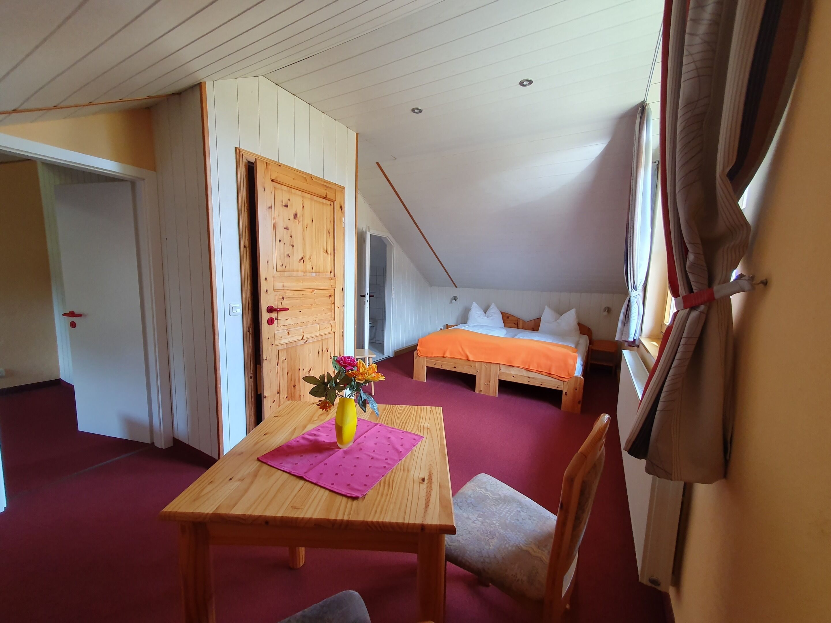 A room with a wooden bed, a wooden table with a vase, and a chair.