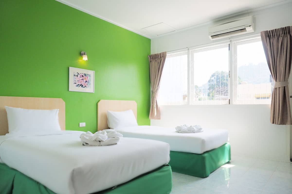 A hotel room with two beds, green walls, a window with curtains, and an air conditioning unit.