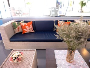 A wicker sofa with dark cushions, a woven side table with a floral arrangement, and a vase with dried flowers.