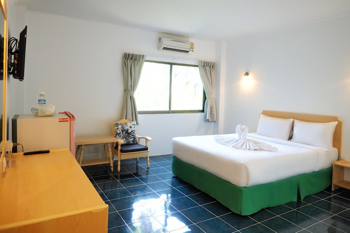 A hotel room with a bed, a desk, a chair, a window with curtains, and an air conditioning unit.