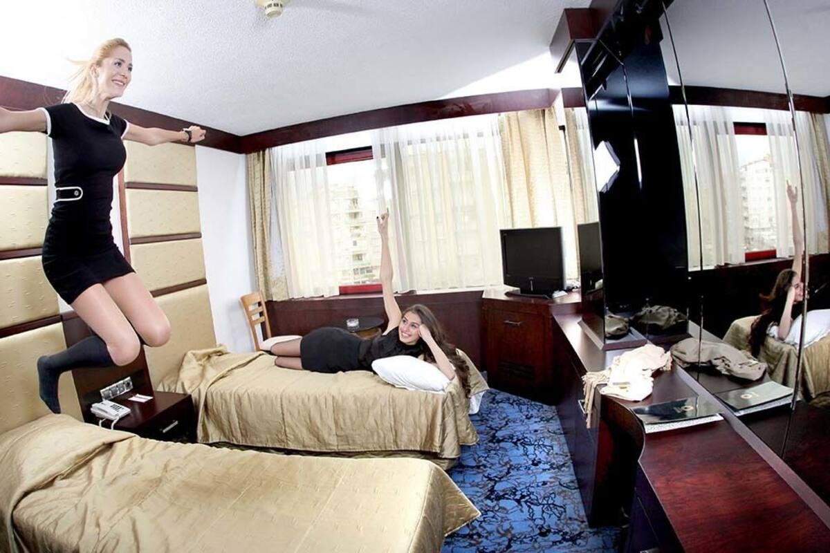 Quarto de hotel com uma cama grande, uma cama menor, uma mesa e uma televisão.