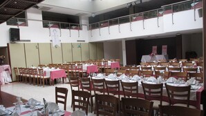 Un salón amplio con varias mesas dispuestas para comer, sillas de madera y una zona de escenario.