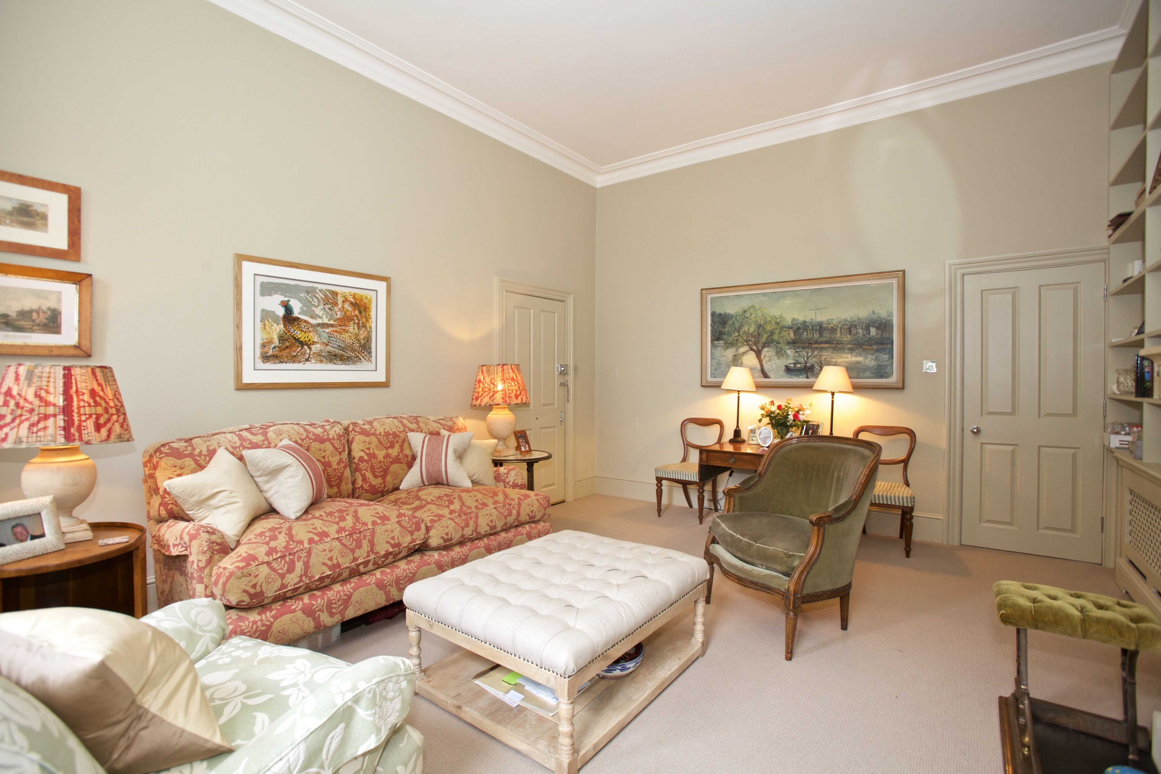A living room with a floral sofa, a tufted ottoman, a green armchair, a wooden coffee table, and two lamps.
