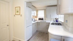 A modern kitchen with white cabinetry, a built-in stove, and a window with blinds. - A Place Like Home - Elegant flat in South Kensington (London)