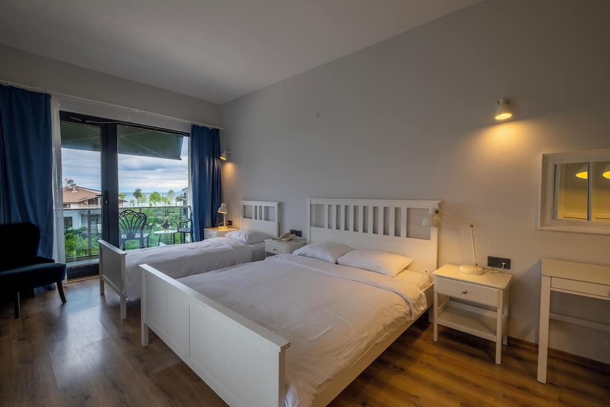 A hotel room with two beds, a desk, a chair, and a large window with curtains.