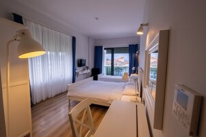 Quarto de hotel com cama, mesa de cabeceira, luminária e vista para edifícios pela janela.