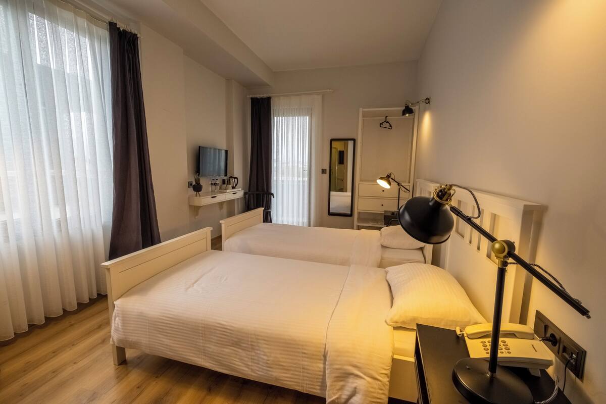 A hotel room with a large bed, bedside table, lamp, and a mirror.