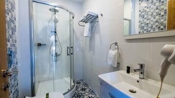 Ein Badezimmer mit Duschkabine, weißem Waschbecken, Fön und Fliesenboden mit Muster.