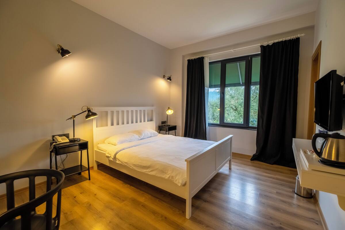 A neatly arranged bedroom with a bed, bedside tables, a chair, a desk, and a window with curtains.