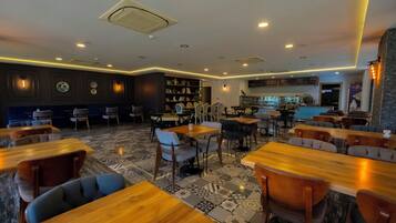 A restaurant with wooden tables and chairs, a patterned floor, and a kitchen area in the background.