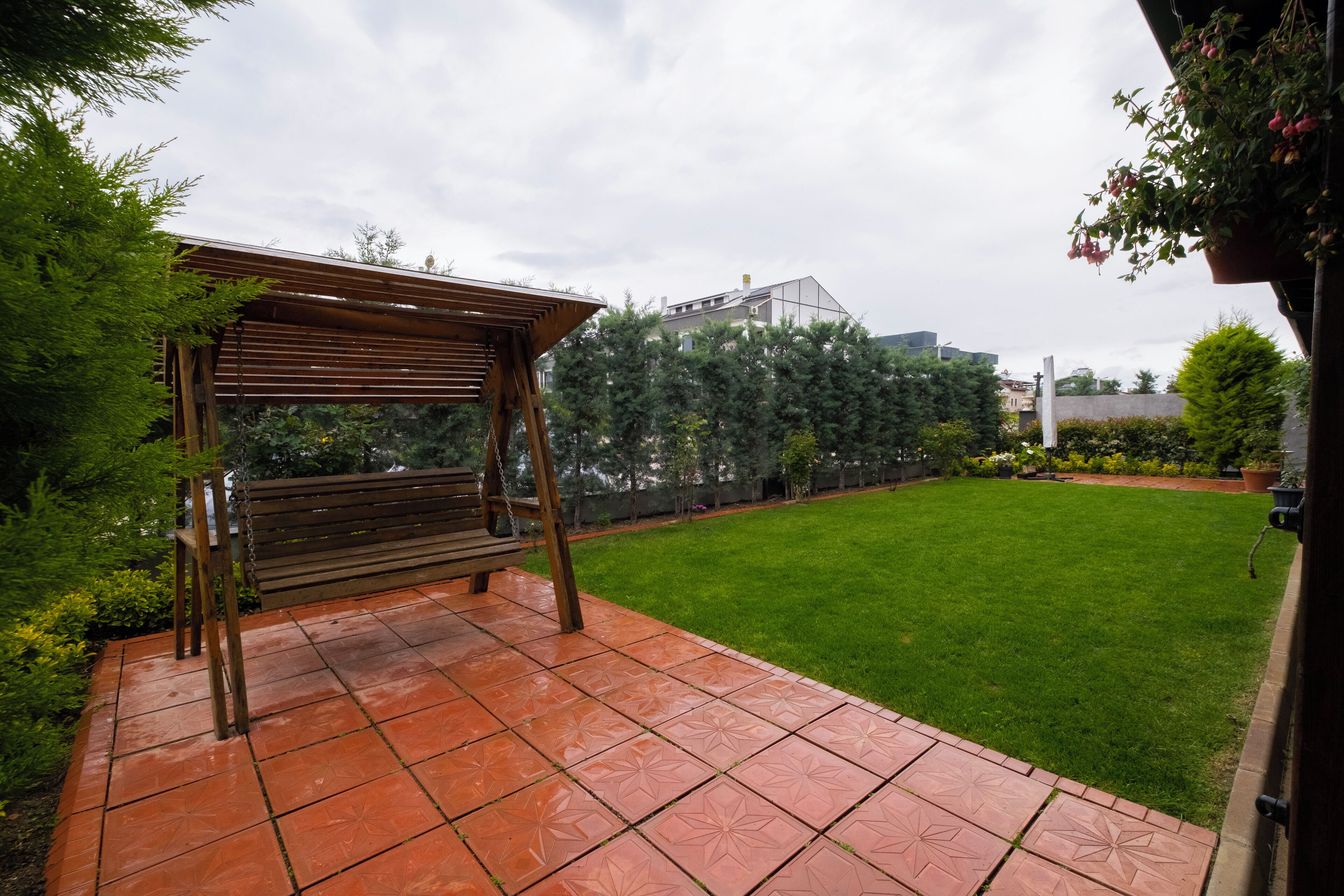 A patio with a wooden pergola, a grassy lawn, and a tiled floor.
