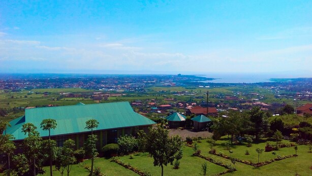 An aerial view of a coastal town with a prominent building with a green roof, surrounded by well-maintained gardens and a clear view of the sea and distant cityscape. - Lago Resort (Kisumu)