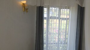 A neatly made bed with white bedding and blue accents, a wall-mounted light, and a window with curtains. - Lago Resort (Kisumu)