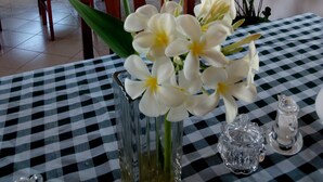 A dining area with checkered tablecloths, a vase with white flowers, and a large window with curtains. - Lago Resort (Kisumu)