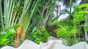 A pathway leading through a lush garden with various tropical plants and a white, pebble-textured floor. - Medori Villa (Seminyak)