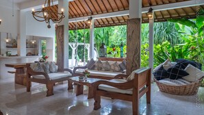 A spacious living area with wooden furniture, a ceiling fan, and a view of lush greenery. - Medori Villa (Seminyak)