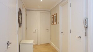 A narrow hallway with white walls, a wooden floor, and a white door at the end. - A Place Like Home - Chelsea Apartment with River Views (London)