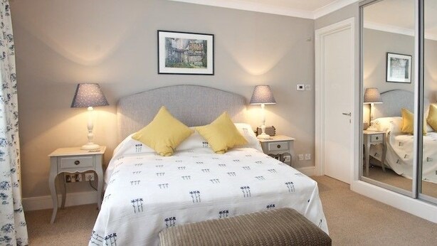 A bedroom with a bed, bedside tables, lamps, a mirror, and a bench. - A Place Like Home - Chelsea Apartment with River Views (London)
