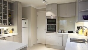 A modern kitchen with white cabinets, a microwave, a refrigerator, and an oven. - A Place Like Home - Chelsea Apartment with River Views (London)