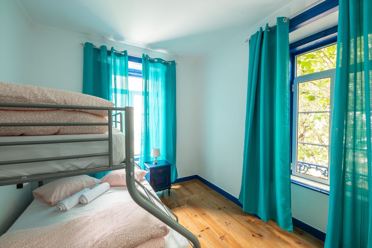 A room with bunk beds, a small table with a lamp, and a window with curtains.