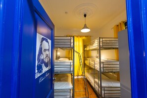 A dormitory room with bunk beds, a poster on the door, and a ceiling light. - Help Yourself Hostels Parede (Cascais)