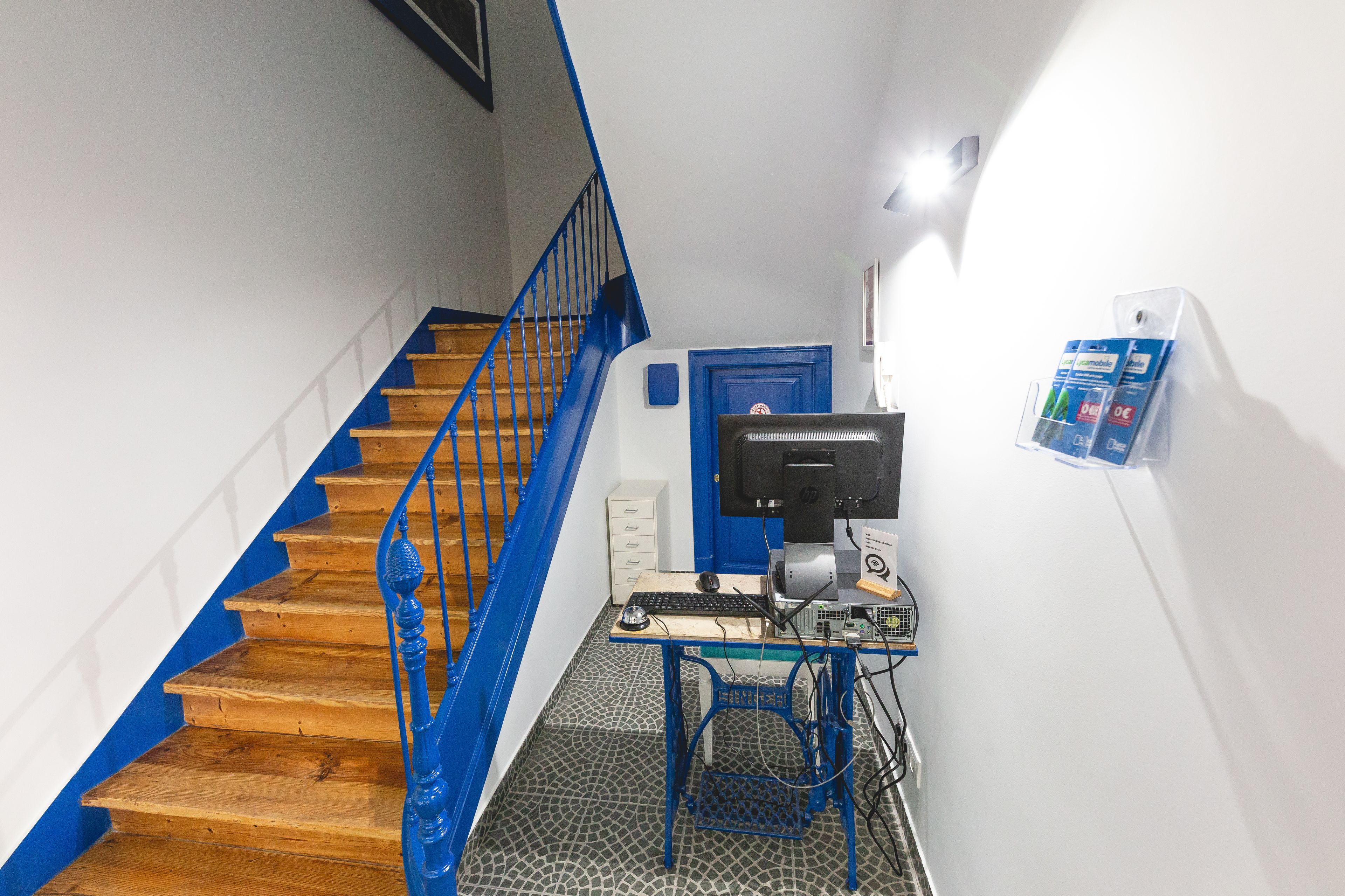 A staircase with blue railings, a desktop computer, and a small desk with a chair.