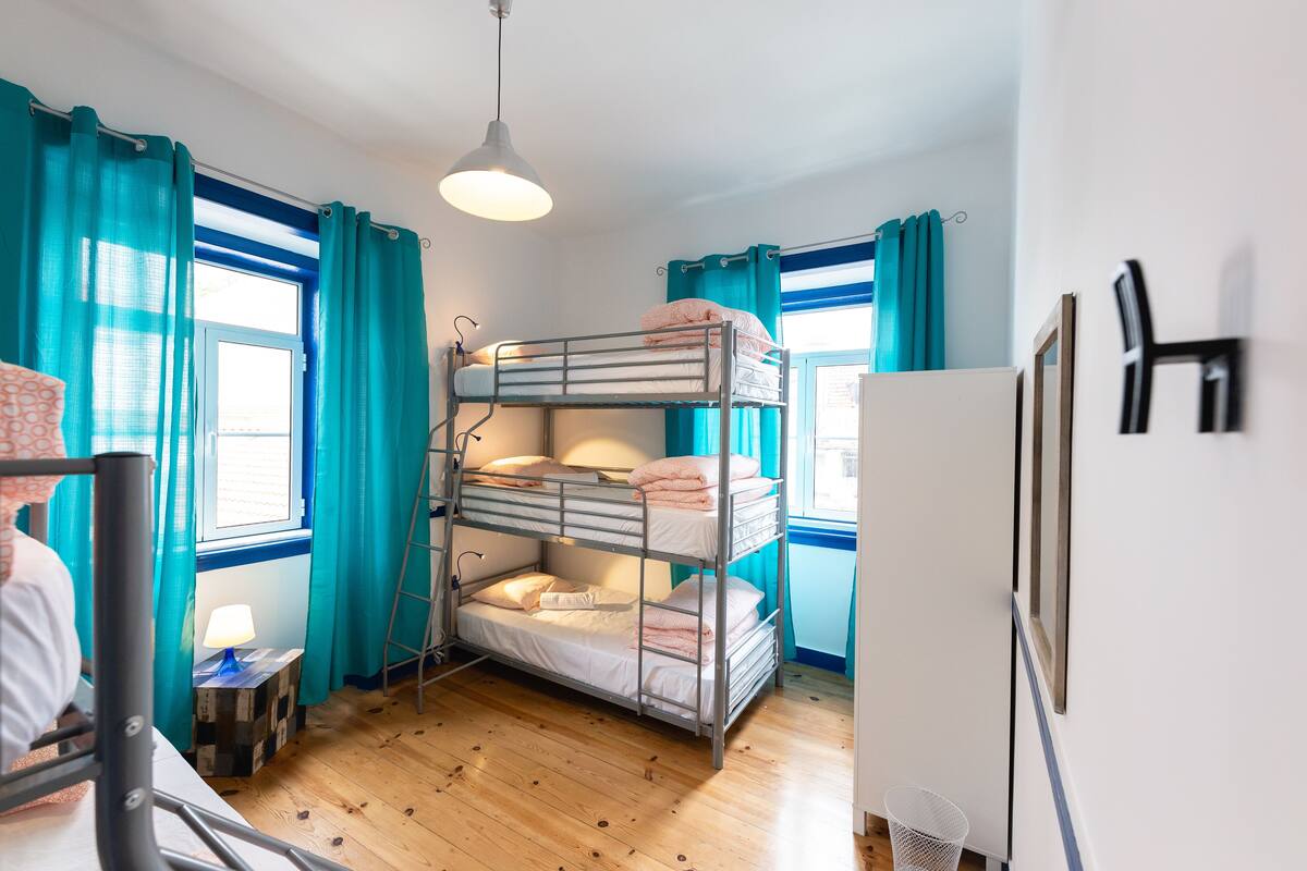 A bunk bed room with a desk, lamp, and window with curtains.