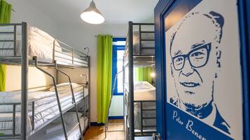 Een studentenkamer met stapelbedden, een trapje, een hanglamp en een poster met een afbeelding van iemand.