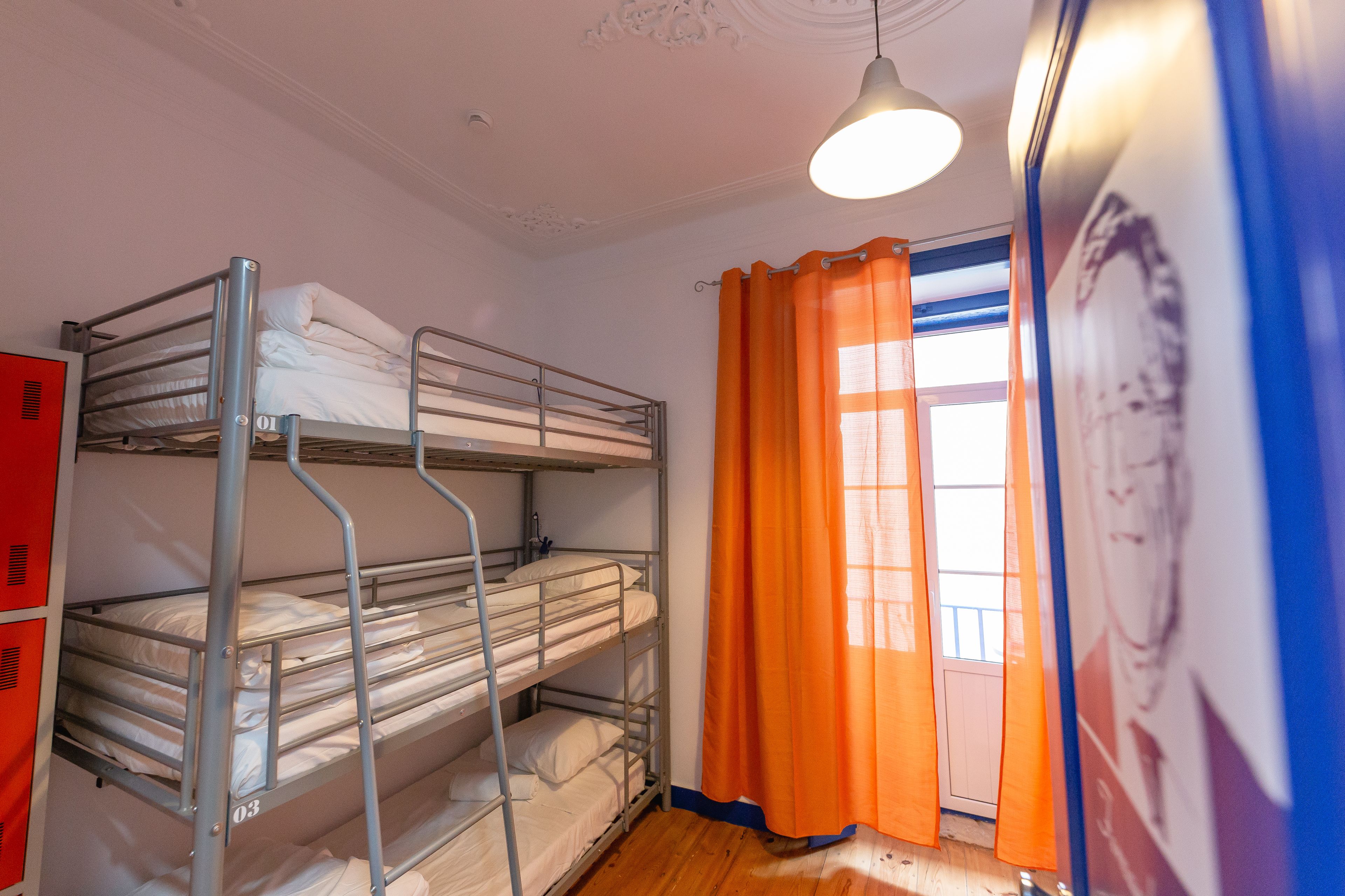 Ett studentrum med våningssängar, ett fönster med orange gardiner och en affisch på väggen.