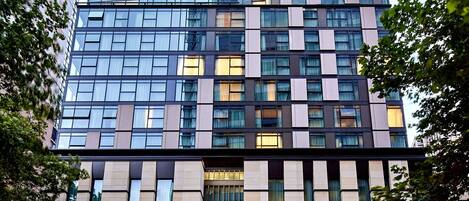 A modern high-rise building with a glass facade, multiple floors, and a ground-level entrance with a visible sign.