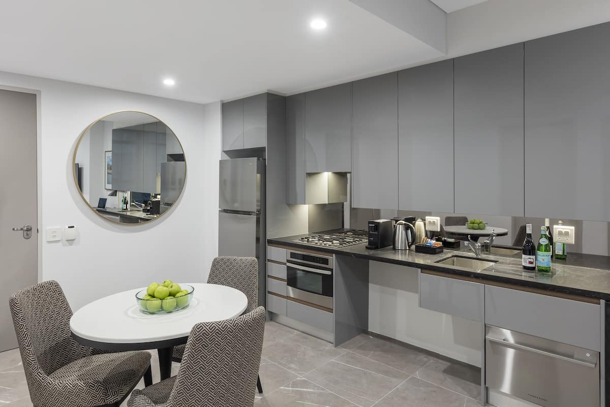 Una cocina moderna con gabinetes grises, electrodomésticos de acero inoxidable, un espejo redondo y un comedor con sillas estampadas.