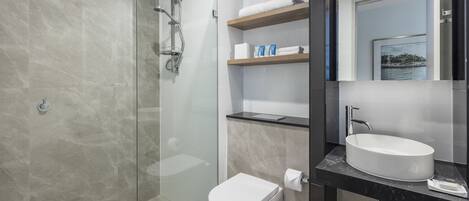 Un baño moderno con ducha de vidrio, inodoro blanco y tocador con lavamanos y espejo.